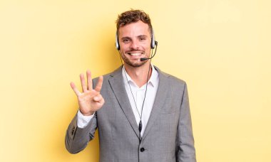 Genç yakışıklı adam gülümsüyor ve arkadaş canlısı görünüyor, dört numarayı gösteriyor. Tele-pazarlamacı ortak.