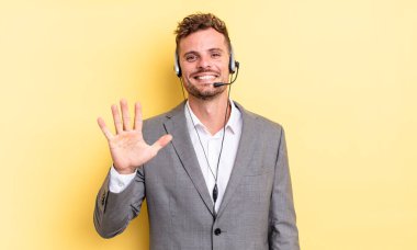 Genç yakışıklı adam gülümsüyor ve arkadaş canlısı görünüyor, beş numarayı gösteriyor. Tele-pazarlamacı ortak.