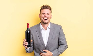 Genç yakışıklı bir adam komik bir şakaya yüksek sesle gülüyor. Şarap şişesi konsepti