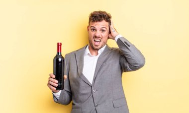 Genç ve yakışıklı bir adam stresli, endişeli ya da korkmuş hissediyor. Elleri başının üstünde. Şarap şişesi konsepti