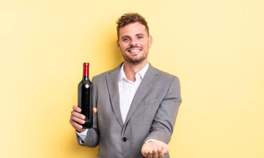 Genç ve yakışıklı bir adam arkadaşça gülümsüyor ve bir konsept sunuyor. Şarap şişesi konsepti
