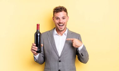Genç ve yakışıklı bir adam mutlu hissediyor ve heyecanla kendini işaret ediyor. Şarap şişesi konsepti