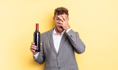 Genç, yakışıklı adam şok olmuş, korkmuş ya da korkmuş görünüyor. Şarap şişesi konsepti