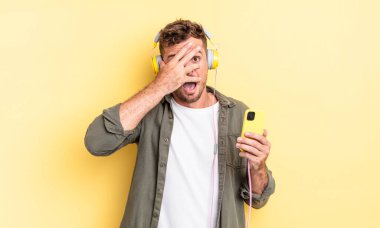 Genç, yakışıklı adam şok olmuş, korkmuş ya da korkmuş görünüyor. Yüzü kulaklıklarla ve akıllı telefon konseptiyle örtülmüş.