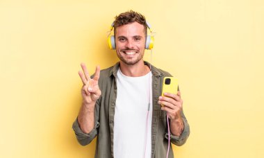 Genç yakışıklı adam gülümsüyor ve arkadaş canlısı görünüyor, üç numaralı kulaklığı ve akıllı telefon konseptini gösteriyor.
