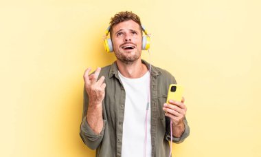 Genç ve yakışıklı adam umutsuz, sinirli ve stresli kulaklıklar ve akıllı telefon konsepti