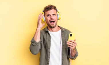 Genç yakışıklı adam eller havada kulaklıklar ve akıllı telefon konseptiyle bağırıyor.