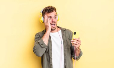 Genç yakışıklı adam mutlu, heyecanlı ve şaşırmış kulaklıklar ve akıllı telefon konsepti