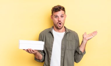 Genç, yakışıklı adam şaşırmış ve şok olmuş görünüyor. Çenesi düşmüş, elinde bir nesne var. beyaz kutu kavramı