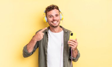 Genç yakışıklı adam, kendine güvenerek gülümseyerek kendi gülümseme kulaklığını ve akıllı telefon konseptini işaret ediyor.