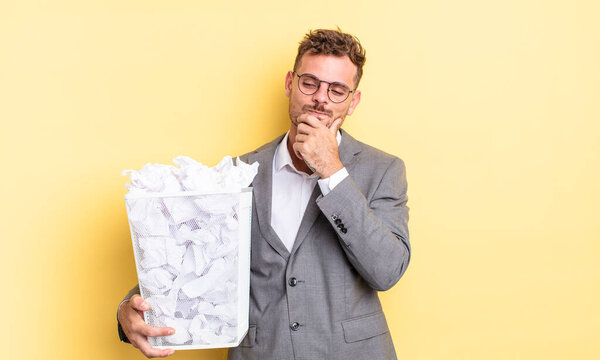 young handsome man smiling with a happy, confident expression with hand on chin paper balls trash concept