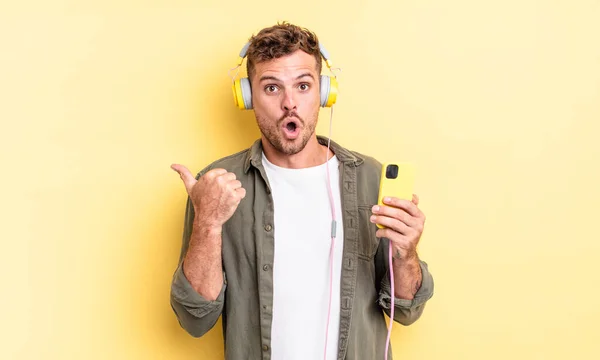 Ung Stilig Man Ser Förvånad Över Misstro Hörlurar Och Smartphone — Stockfoto