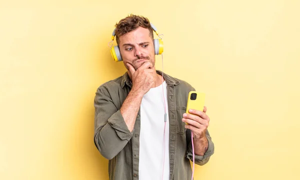 Młody Przystojny Mężczyzna Myśli Uczucie Wątpliwości Zdezorientowany Słuchawki Koncepcja Smartfona — Zdjęcie stockowe