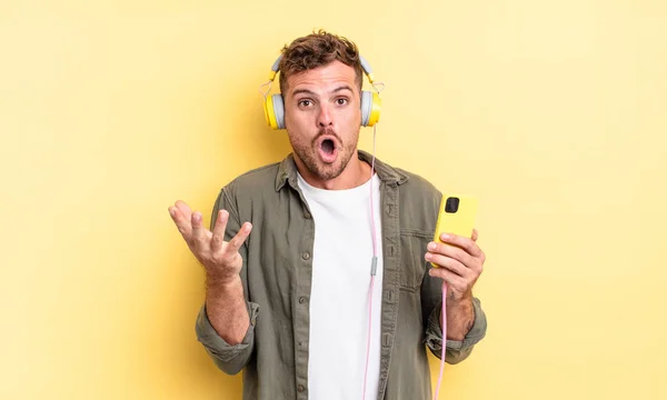 Mladý Pohledný Muž Pocit Velmi Šokovaný Překvapený Sluchátka Smartphone Koncept — Stock fotografie