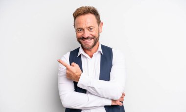 Orta yaşlı yakışıklı adam neşeli bir şekilde gülümsüyor, mutlu hissediyor ve bir tarafı işaret ediyor.