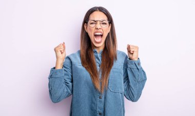 Güzel İspanyol bir kadın kızgın bir ifadeyle agresif bir şekilde bağırıyor ya da yumruklarıyla başarıyı kutluyor.