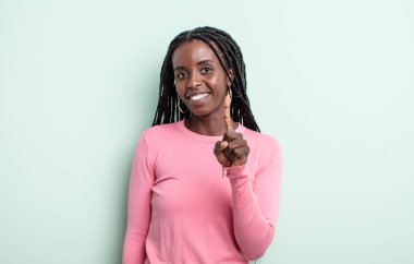 Siyah, güzel bir kadın gülümsüyor ve arkadaş canlısı görünüyor. Bir numarayı gösteriyor ya da ilk eli önde, geri sayıyor.