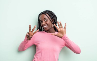 Siyah, güzel bir kadın gülümsüyor ve arkadaş canlısı görünüyor, 8 ya da 8 numarayı gösteriyor, elleri önde, geriye doğru sayıyor.