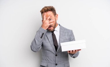 Orta yaşlı yakışıklı bir adam şok olmuş, korkmuş ya da korkmuş görünüyor. Yüzü elle kapatılmış. beyaz paket kavramı