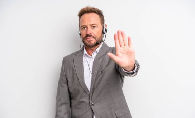 Orta yaşlı yakışıklı adam ciddi görünüyor. Avuç içi gösteriyor. Durdurma hareketi yapıyor. tele pazarlama kavramı
