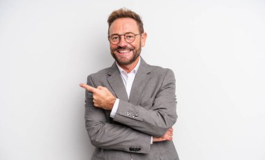 Orta yaşlı yakışıklı bir adam neşeli bir şekilde gülümsüyor, mutlu hissediyor ve bir tarafı işaret ediyor. İş adamı konsepti