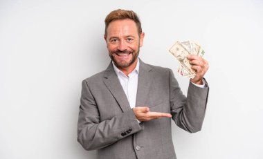 Orta yaşlı yakışıklı adam neşeli bir şekilde gülümsüyor, mutlu hissediyor ve bir konsept gösteriyor. Dolar banknotları konsepti