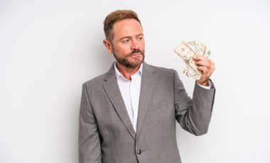Orta yaşlı yakışıklı bir adam üzgün, üzgün ya da kızgın hissedip yan tarafa bakıyor. Dolar banknotları konsepti