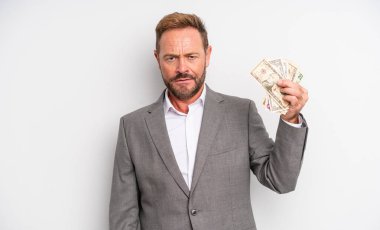 Orta yaşlı yakışıklı bir adam kafası karışık ve şaşkın hissediyor. Dolar banknotları konsepti
