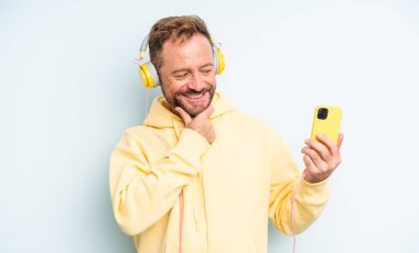 Orta yaşlı yakışıklı, gülümseyen, kendine güvenen, elleri çenesinde bir adam. kulaklıklar ve akıllı telefon konsepti