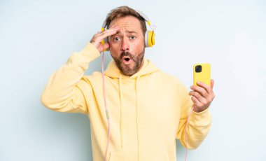 Orta yaşlı yakışıklı adam mutlu, şaşkın ve şaşırmış görünüyor. kulaklıklar ve akıllı telefon konsepti