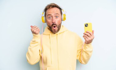 Orta yaşlı yakışıklı bir adam inançsızlıktan şaşkın şaşkın bakıyor. kulaklıklar ve akıllı telefon konsepti