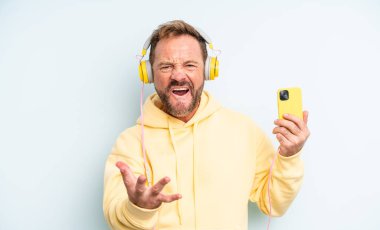 Orta yaşlı yakışıklı bir adam sinirli, sinirli ve sinirli görünüyor. kulaklıklar ve akıllı telefon konsepti