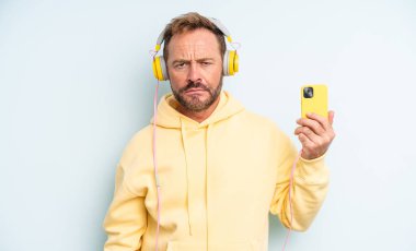 Orta yaşlı, yakışıklı, üzgün ve mızmız, mutsuz bakışlı ve ağlayan bir adam. kulaklıklar ve akıllı telefon konsepti