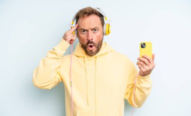 Orta yaşlı yakışıklı adam şaşırmış görünüyor, yeni bir düşünce, fikir ya da konsept keşfediyor. kulaklıklar ve akıllı telefon konsepti