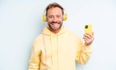 Orta yaşlı yakışıklı adam mutlu ve hoş bir şekilde şaşırmış görünüyor. kulaklıklar ve akıllı telefon konsepti