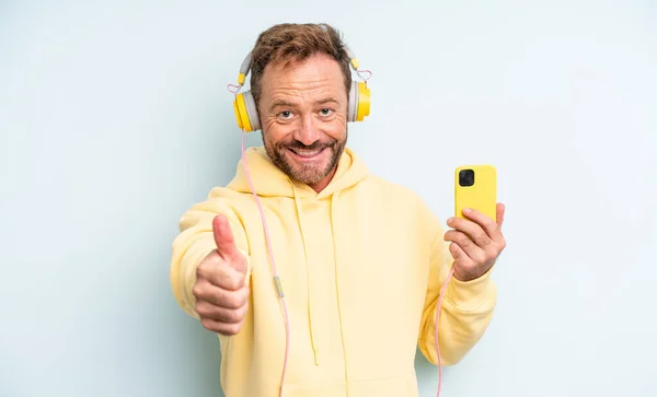 中年英俊男子感到自豪 微笑着竖起大拇指 耳机和智能手机的概念 — 图库照片