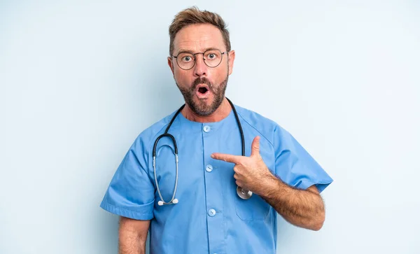 중년의 잘생긴 남자가 자신을 가리키며 벌리고 과놀란 표정을 있습니다 간호사 — 스톡 사진