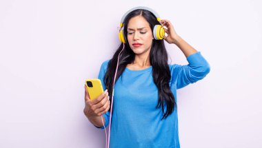 Kafası karışık, kafası karışık, kaşınan bir İspanyol kadın. akıllı telefon ve kulaklık kavramı