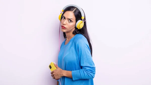 かなりヒスパニック系の女性は悲しい 動揺や怒りを感じ 側を探しています スマートフォンとヘッドフォンのコンセプト — ストック写真