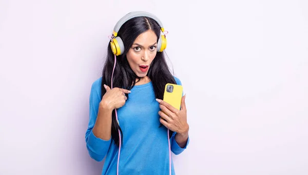 かなりヒスパニック系の女性ショックを受けて 口を大きく開いて驚いて 自分自身を指している スマートフォンとヘッドフォンのコンセプト — ストック写真