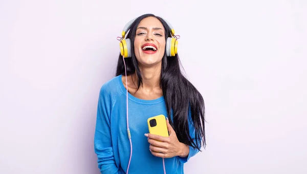かなりヒスパニック系の女性が幸せそうな驚きを見て スマートフォンとヘッドフォンのコンセプト — ストック写真