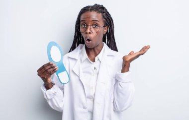 Güzel siyah kadın şaşırmış ve şok olmuş görünüyor. Çenesi düşmüş ve elinde bir nesne tutuyor. podiatrist kavramı