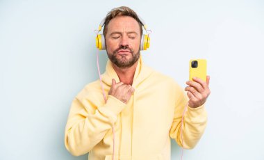 Orta yaşlı yakışıklı bir adam stresli, endişeli, yorgun ve hayal kırıklığına uğramış hissediyor. kulaklıklar ve akıllı telefon konsepti