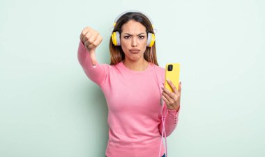 Güzel İspanyol bir kadın kendini kötü hissediyor, baş parmağını kaldırıyor. akıllı telefon ve kulaklık kavramı