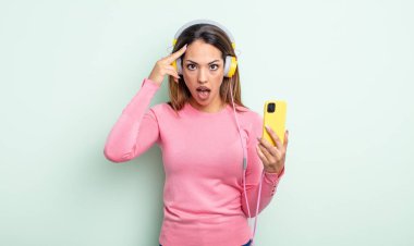Yeni bir düşünce, fikir ya da konsept edinen oldukça İspanyol bir kadın şaşırmış görünüyor. akıllı telefon ve kulaklık kavramı