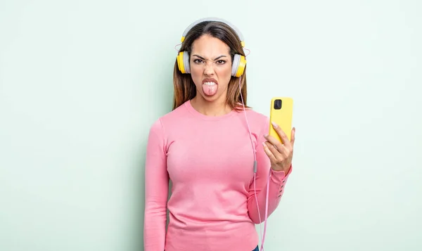 Pěkně Hispánská Žena Znechucená Podrážděná Vyceněným Jazykem Smartphone Sluchátka Koncept — Stock fotografie