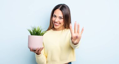 Güzel İspanyol kadın gülümsüyor ve arkadaş canlısı görünüyor, dört numarayı gösteriyor. ev bitkisi kavramı