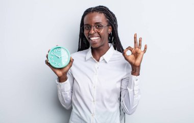 Güzel siyah kadın kendini mutlu hissediyor, iyi bir jestle onaylıyor. Alarm saati kavramı