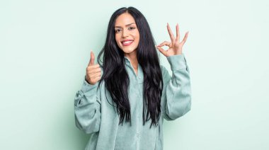 Güzel, İspanyol bir kadın mutlu, şaşkın, tatmin olmuş ve şaşırmış hissediyor, iyi olduğunu gösteriyor ve el kol hareketleri yapıyor, gülümsüyor.