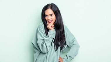 Güzel İspanyol bir kadın mutlu, kendinden emin bir ifadeyle gülümsüyor. Elleri çenesinde, merak ediyor ve yan tarafa bakıyor.